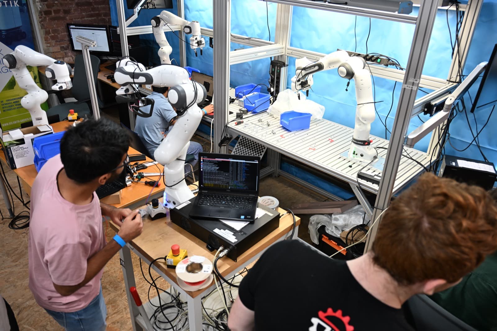 Zwei Personen verkabeln und testen Roboterarme an einer Werkbank