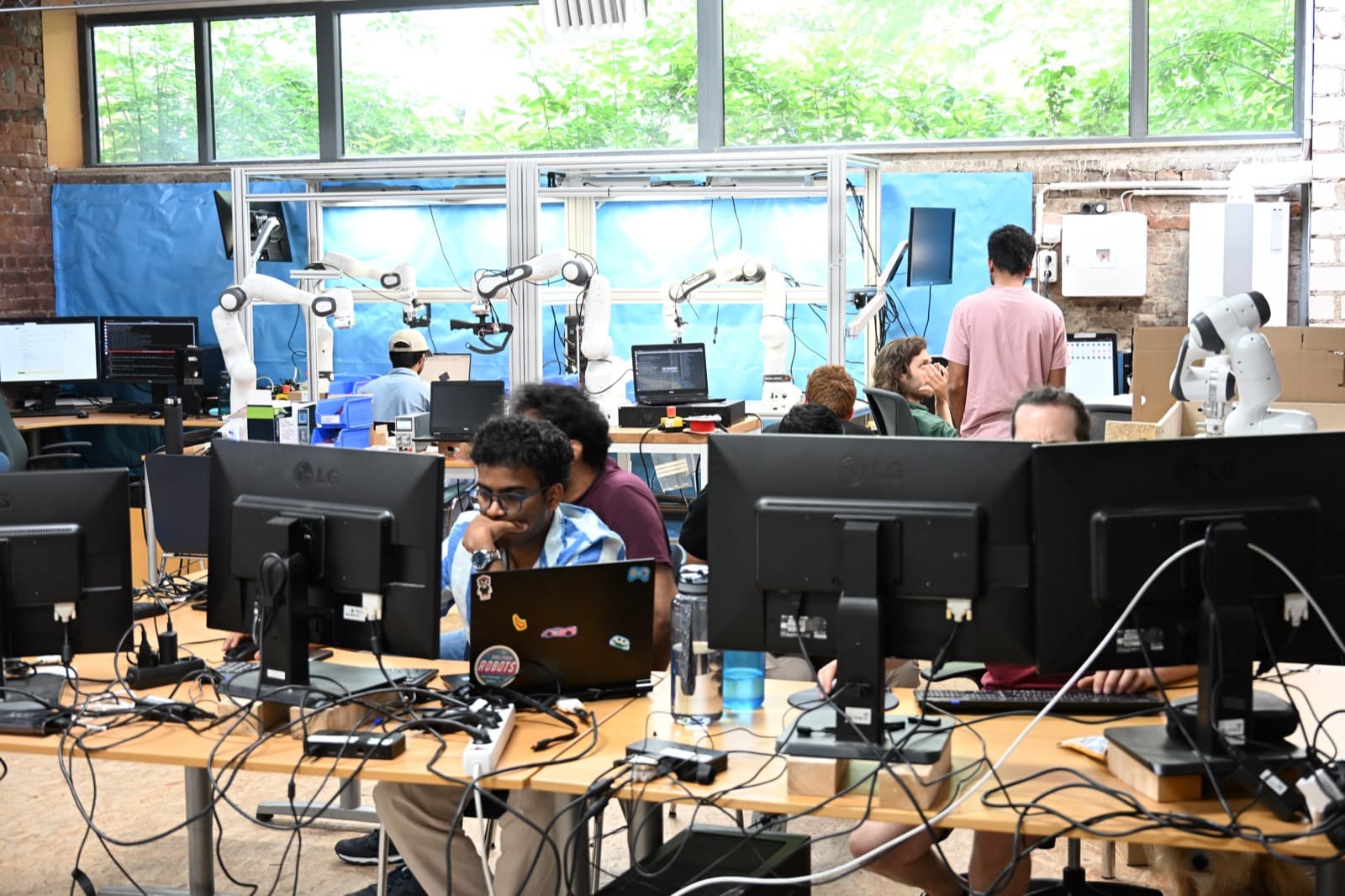 Hackathon-Werkstatt mit Roboterarmen und Teams an ihren Laptops